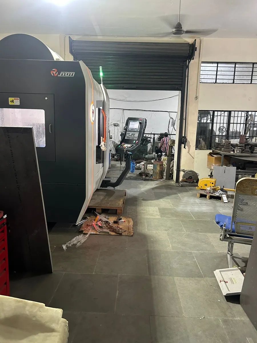 Side view of the machining centre in the workshop bay, with another CNC control panel visible further down the shop.